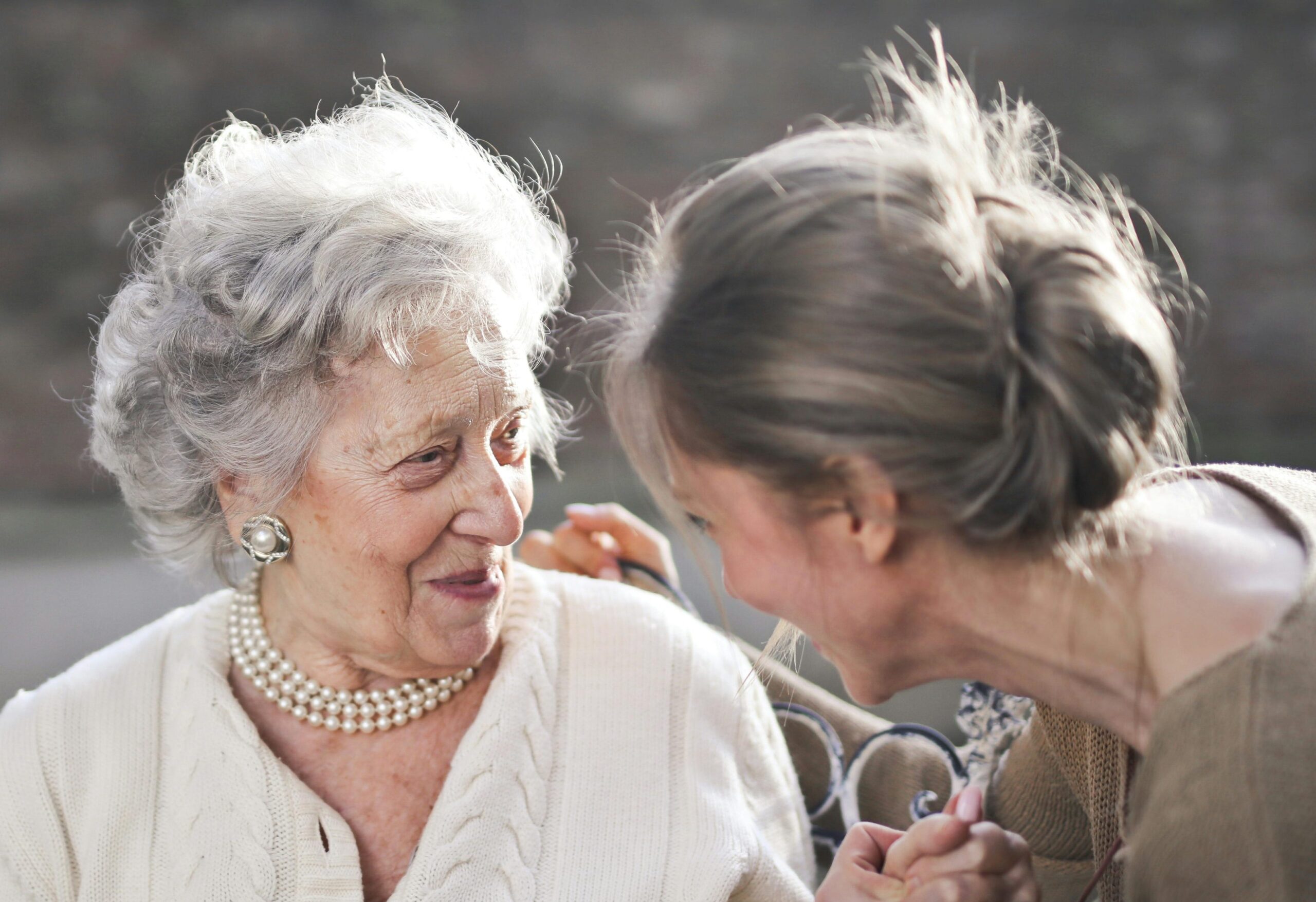pexels-photo-3768114-3768114 Joyful interaction between an elderly woman and her granddaughter in a sunny outdoor setting.